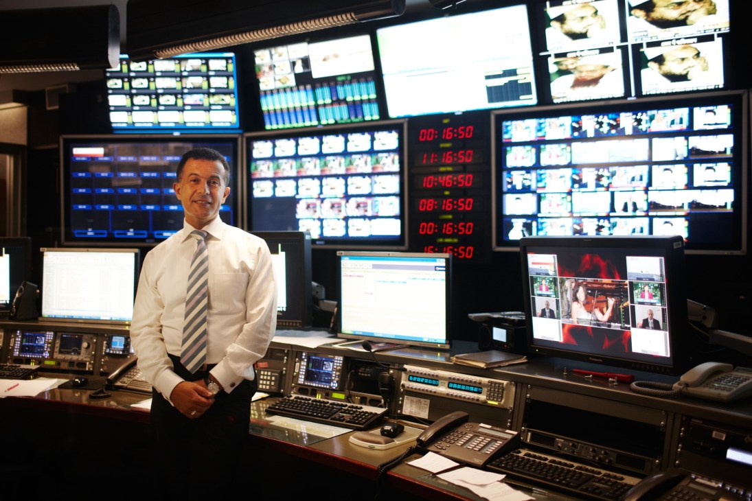 Michael Ebeid, SBS managing director, stands in a TV studio control room surrounded by multiple screens and broadcasting equipment.