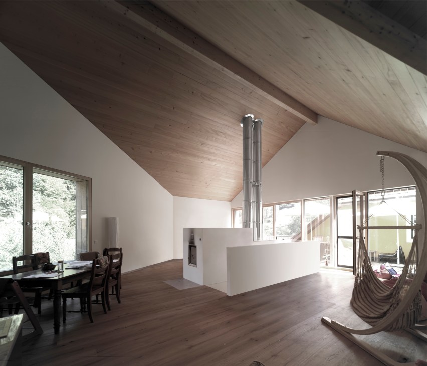 Modern interior with exposed timber ceiling, central fireplace, dining area and hammock in an Austrian distillery and house.