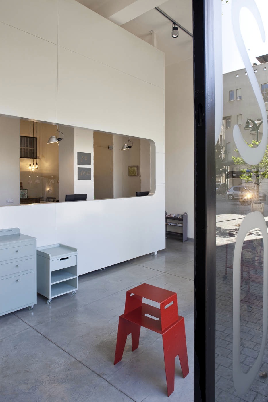 Modern minimalist interior of Rose&Bloom architects office with white reception desk, pendant lights, and red sculptural seating.