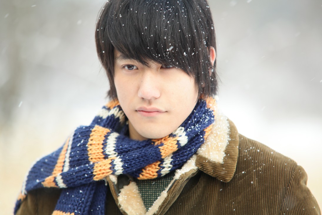 Young person with dark hair wearing a navy and gold argyle scarf in falling snow.