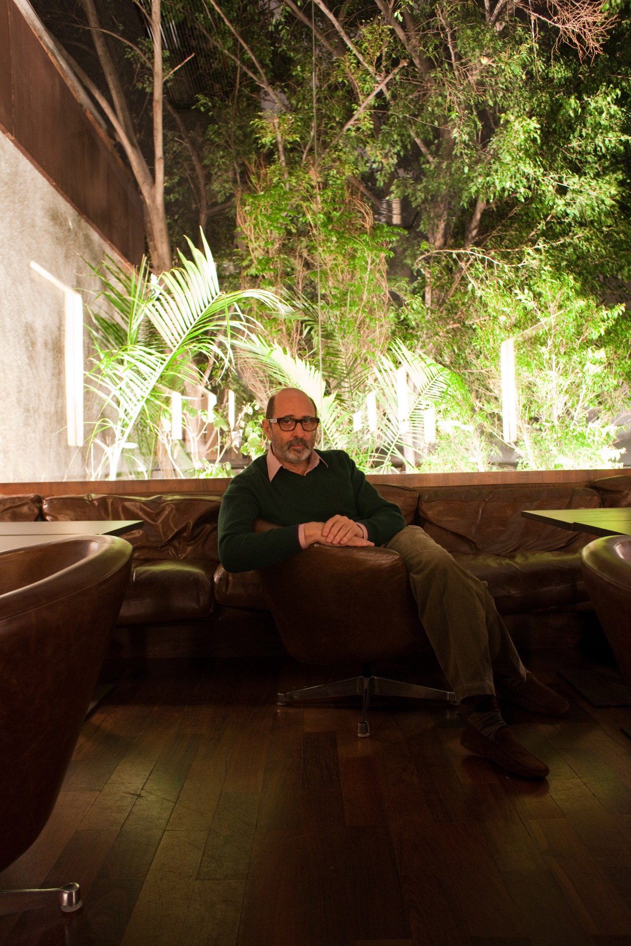Architect Isay Weinfeld sits on a leather sofa in Numero lounge with illuminated garden visible behind him.