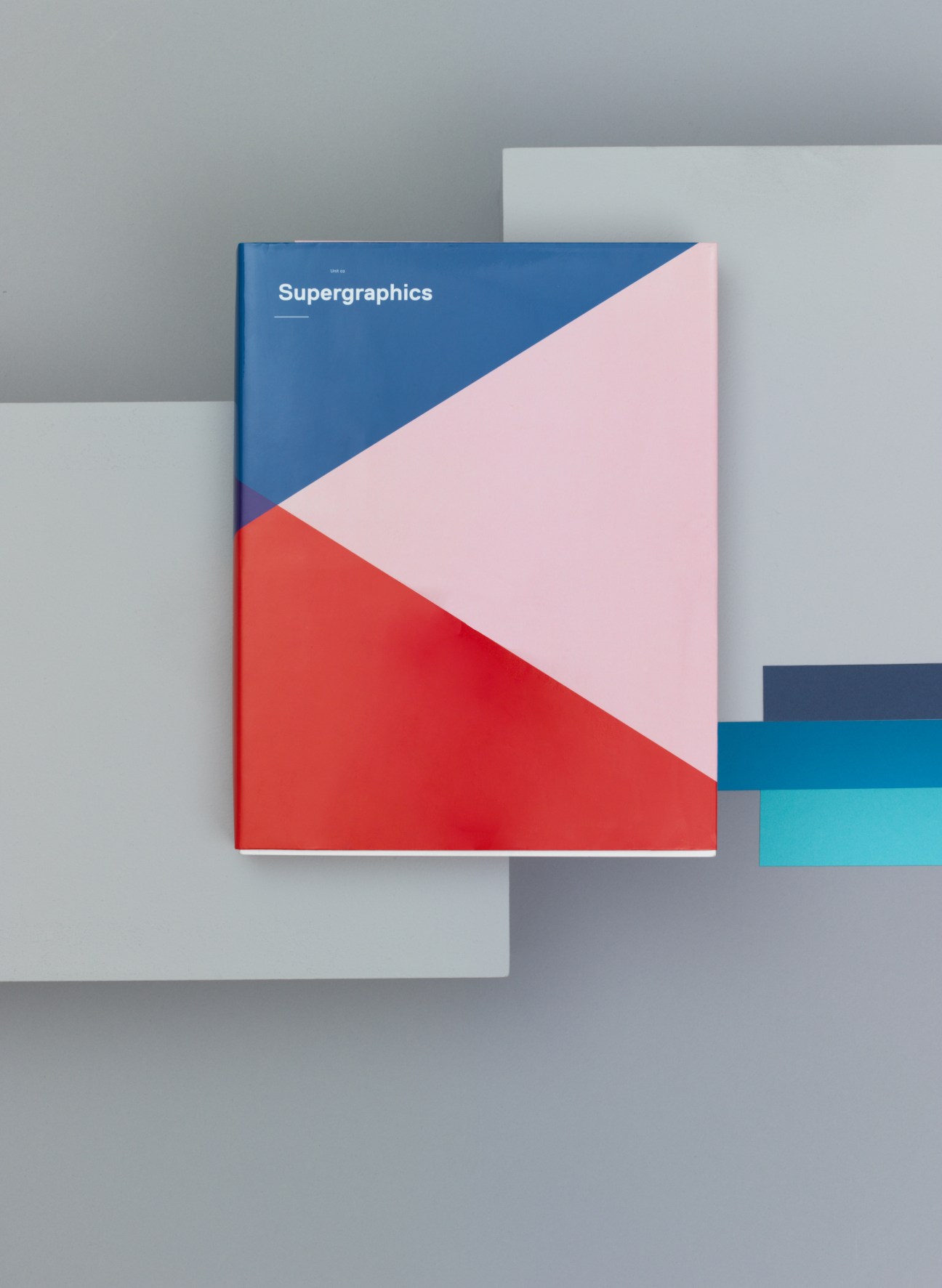 Supergraphics book with blue, pink and red geometric cover design on grey background.