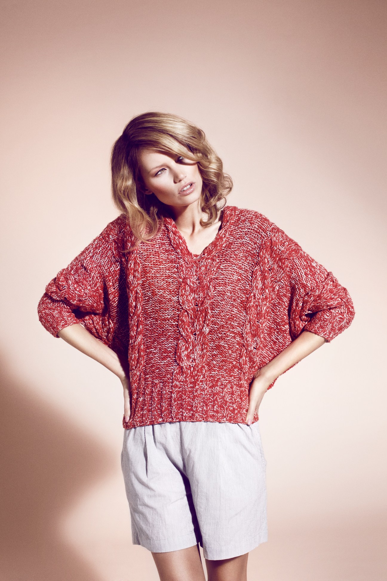 Woman wearing a red cable-knit jumper by Macphee and white shorts by Duša against a neutral background.