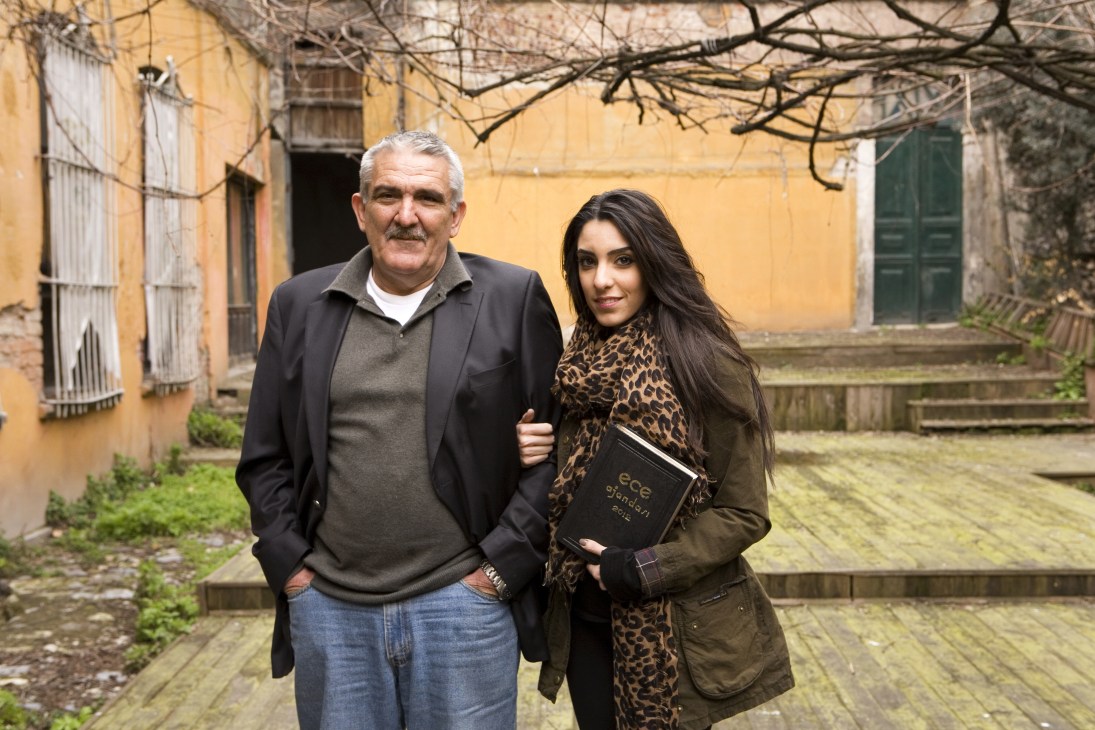 Murat Gunsiray and his daughter Sedef stand in front of a yellow building holding an Ece diary.