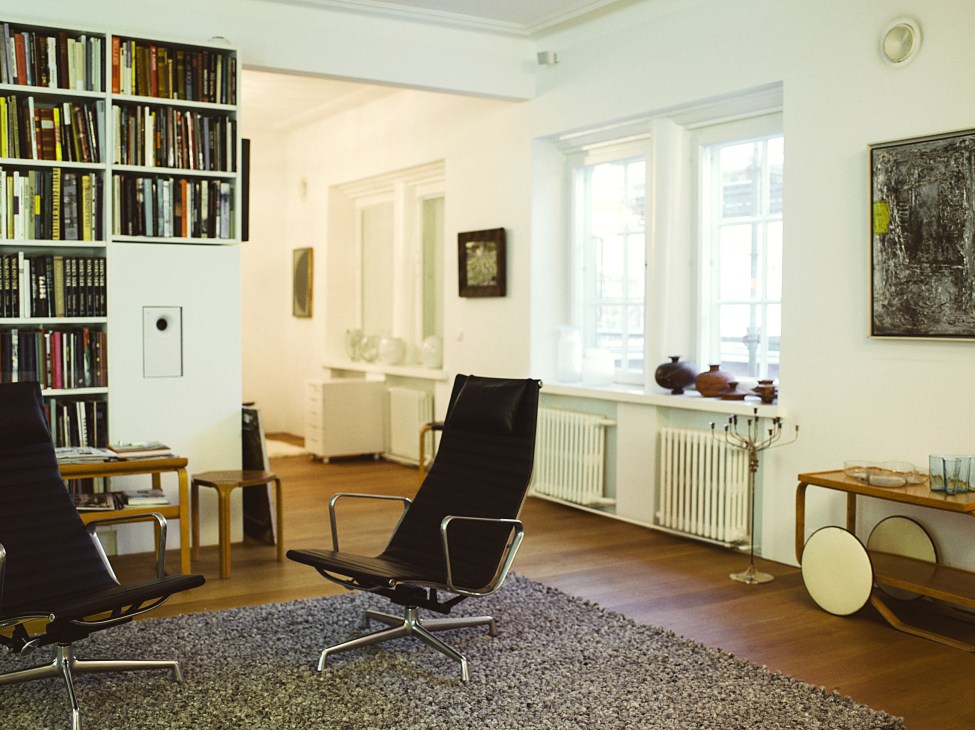 Modern open-plan living room with Charles and Ray Eames Aluminium Group lounge chairs, built-in bookshelves, and minimalist furniture.