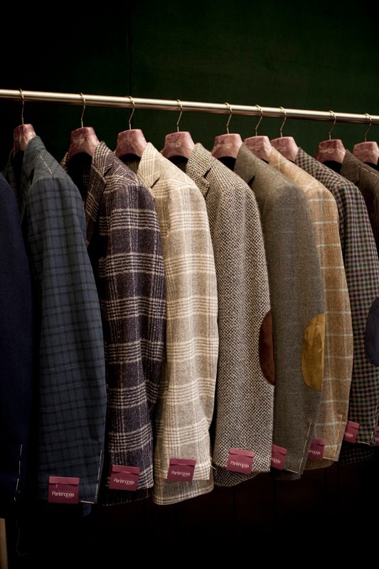 Row of Sartoria Partenopea blazers in various wool textures and patterns hanging on a brass rail.