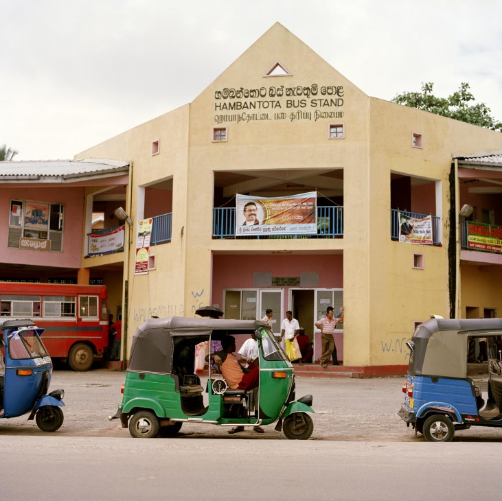 Hambantota Bus Stand with tuk-tuks parked in front and passengers outside the yellow building.