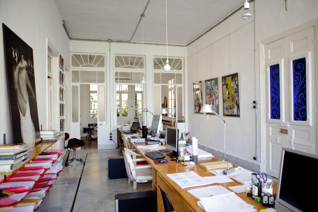 Bright, open-plan architects' office with white doors, wooden desks, red cushions, and artwork on walls.