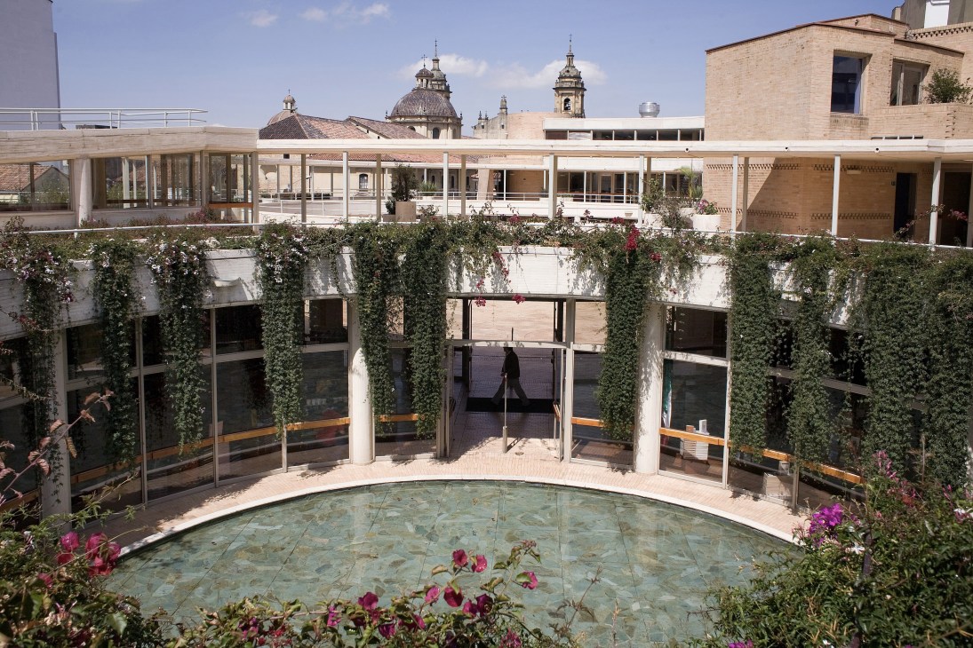 Modern courtyard with central pool, ivy-covered walls and flowering plants, with colonial church domes visible in the background.
