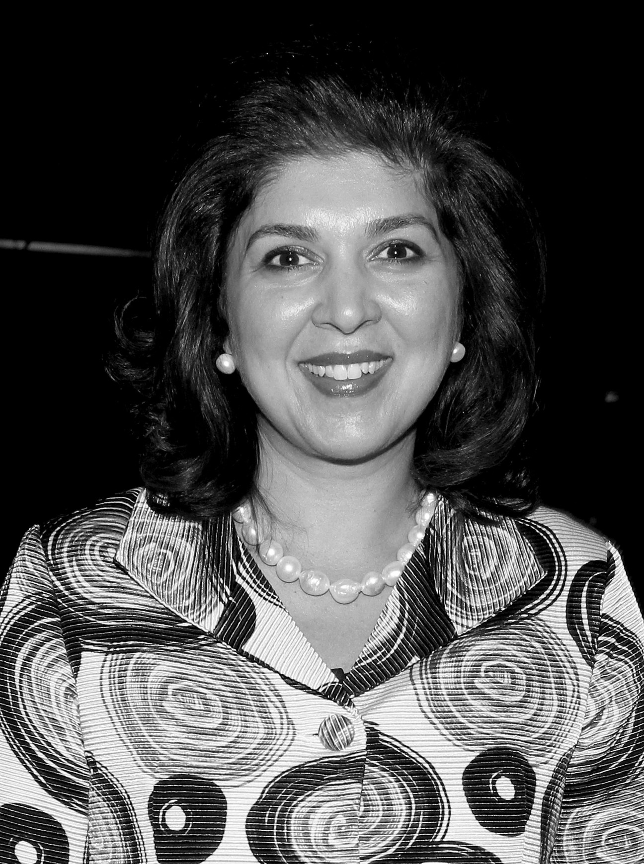 Black and white portrait photograph of Farah Pandith, Special Representative to Muslim Communities, smiling at the camera wearing a patterned jacket and pearl necklace.