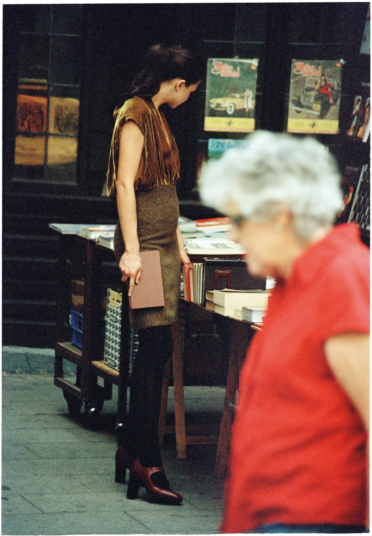 Woman in Prada dress and Marni tights browsing antique books at a Madrid market stall.