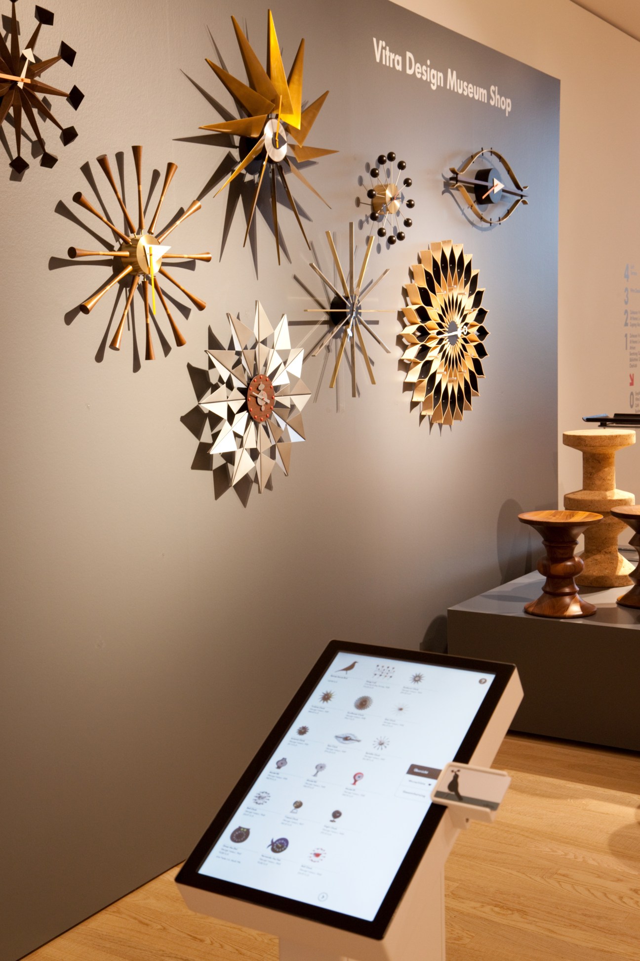 Vitra Design Museum Shop interior displaying geometric clocks and wooden pedestals with digital interactive screen.