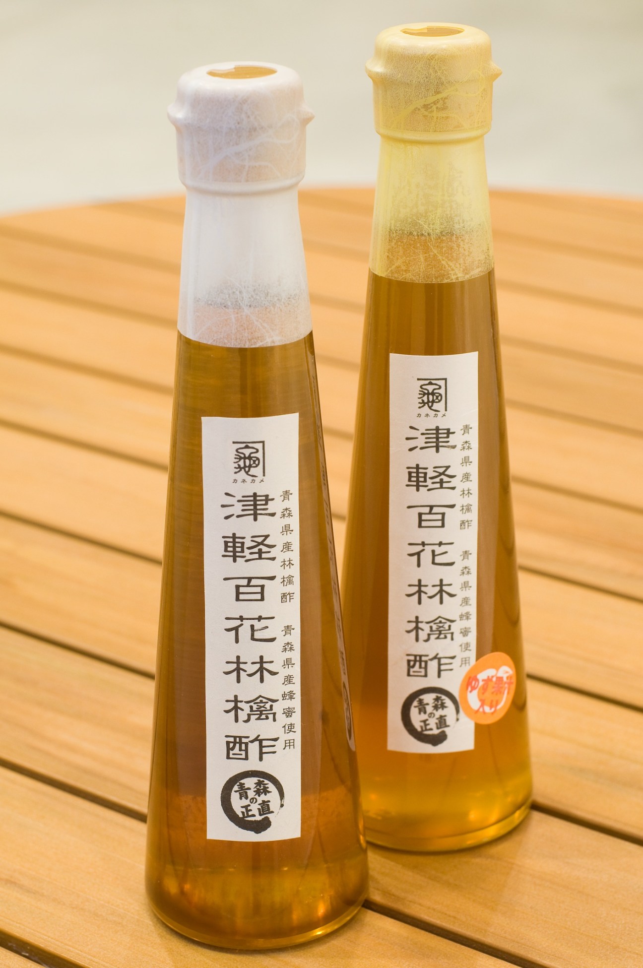 Two bottles of Tsugaru Hyakka vinegar drink with Japanese labels and foam heads on wooden surface.