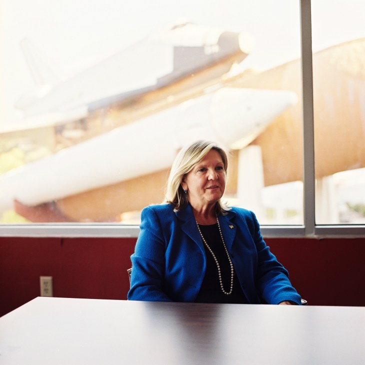 Deborah Barnhart, executive director of the US Space & Rocket Center museum, seated at a table with rocket engines visible through the window behind her.