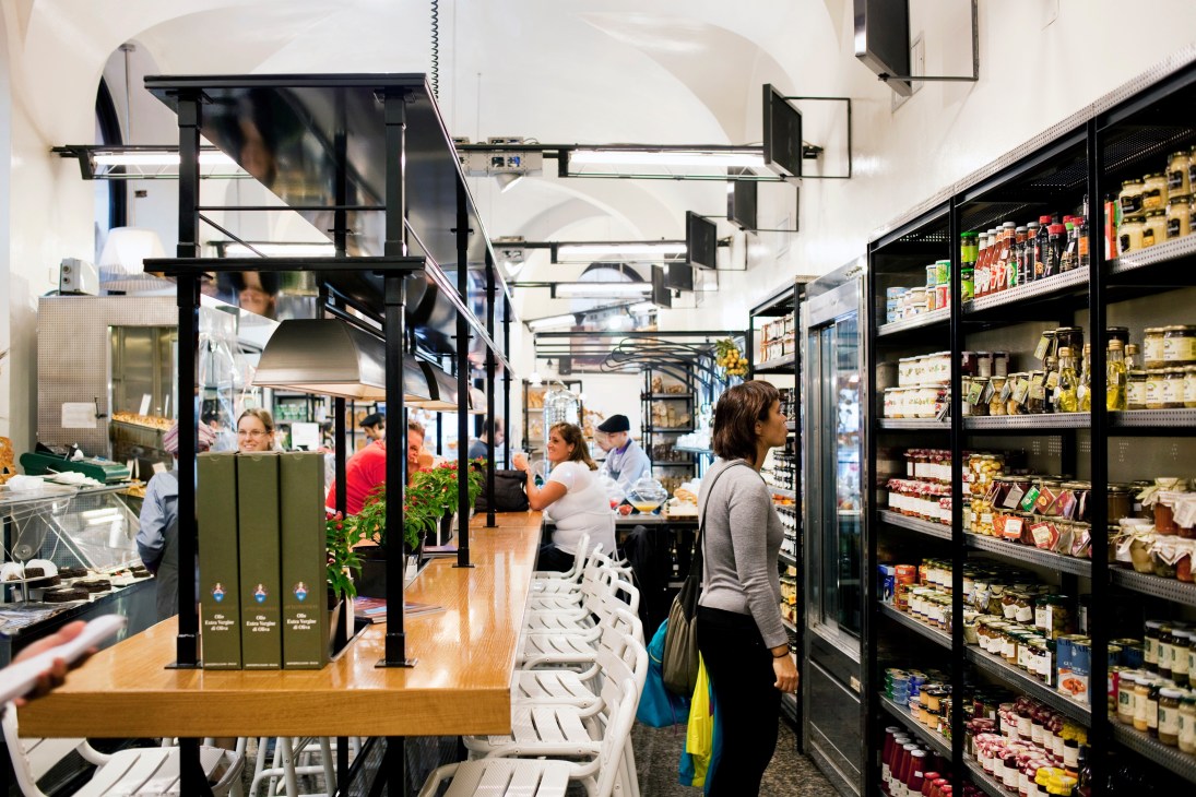 Interior of Panella gourmet bakery with customers shopping among refrigerated cases and shelves of Italian products.