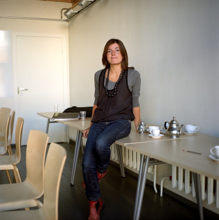 Woman sitting on table in modern office space with tea service.