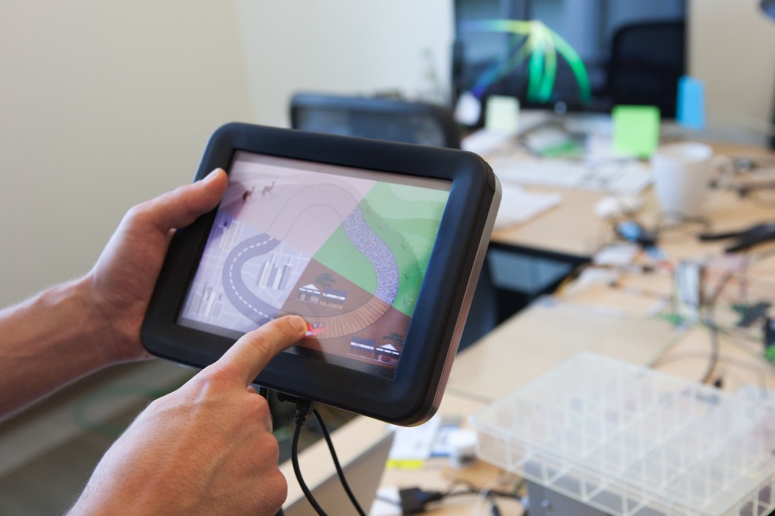 Hands holding tablet displaying Tesla Touch prototype interface at Disney Research workspace.