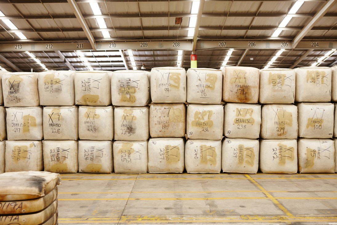 Stacked wool bales marked with identification numbers in a warehouse with industrial ceiling and numbered sections.