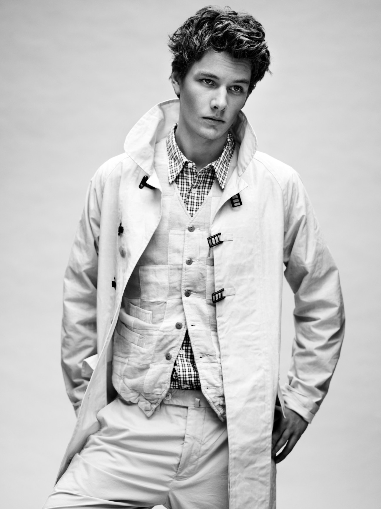 Male model wearing a white Nigel Cabourn coat over a Beams+ waistcoat and Oliver Spencer shirt with checkered collar.