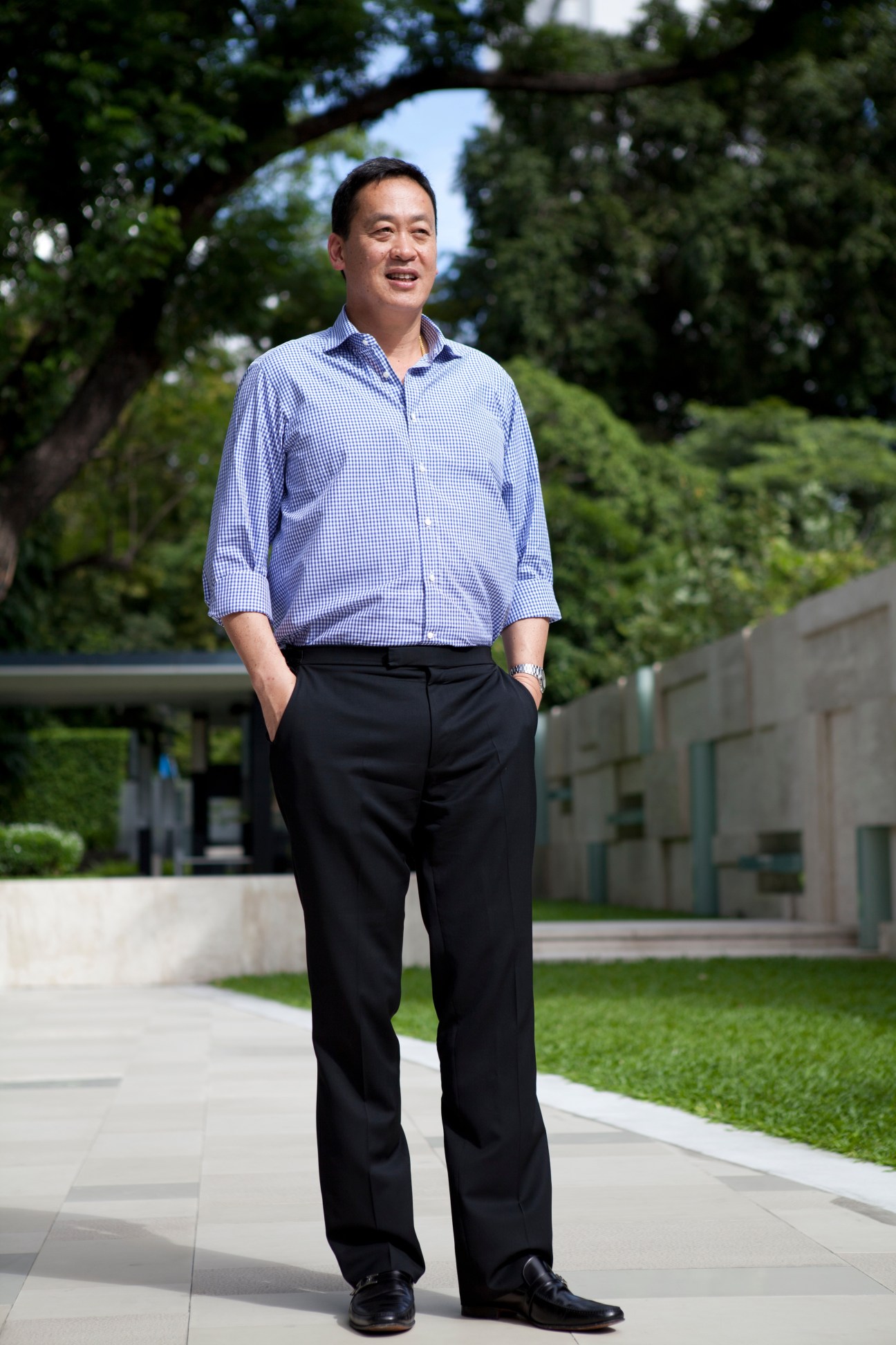 Srettha Thavisin standing outdoors in a blue checkered shirt and black trousers.