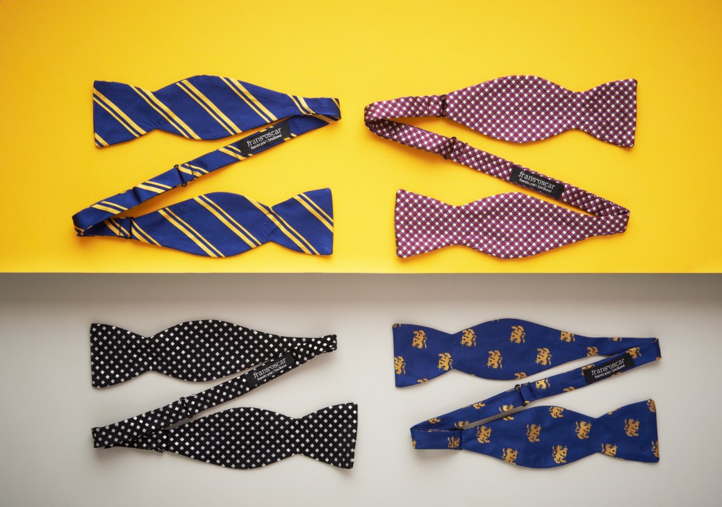 Four colorful bowties displayed on yellow and gray backgrounds, including navy and gold striped, purple checkered, black dotted, and blue patterned designs from Frans Oscar.