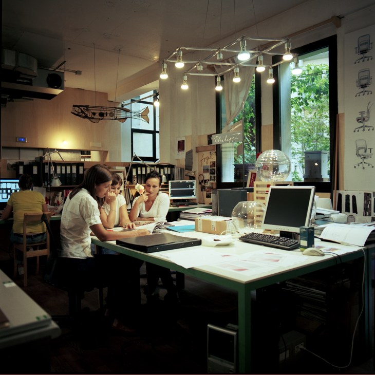 Staff members examine architectural plans at a desk in Michele De Lucchi's Milan studio.