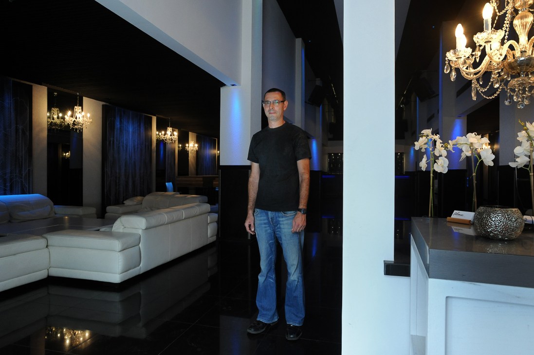 Man standing in modern banquet hall with white furniture, chandeliers and blue lighting