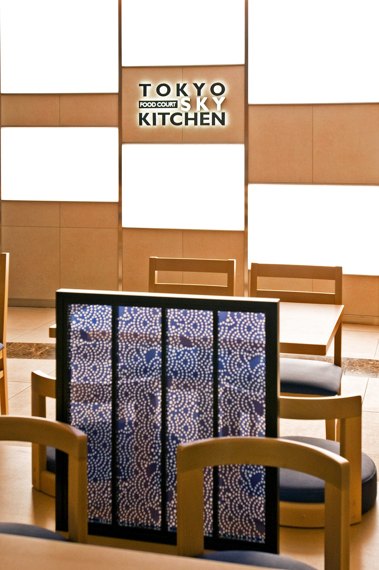 Tokyo Sky Kitchen restaurant signage above seating area with wooden chairs and patterned divider screen.