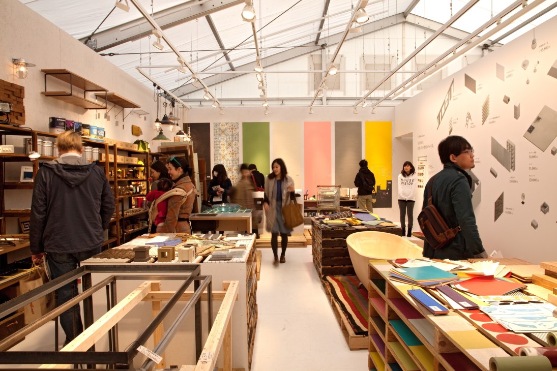 Interior of House Vision exhibition in Tokyo featuring design displays, colorful panels, shelving, and visitors browsing home design materials.