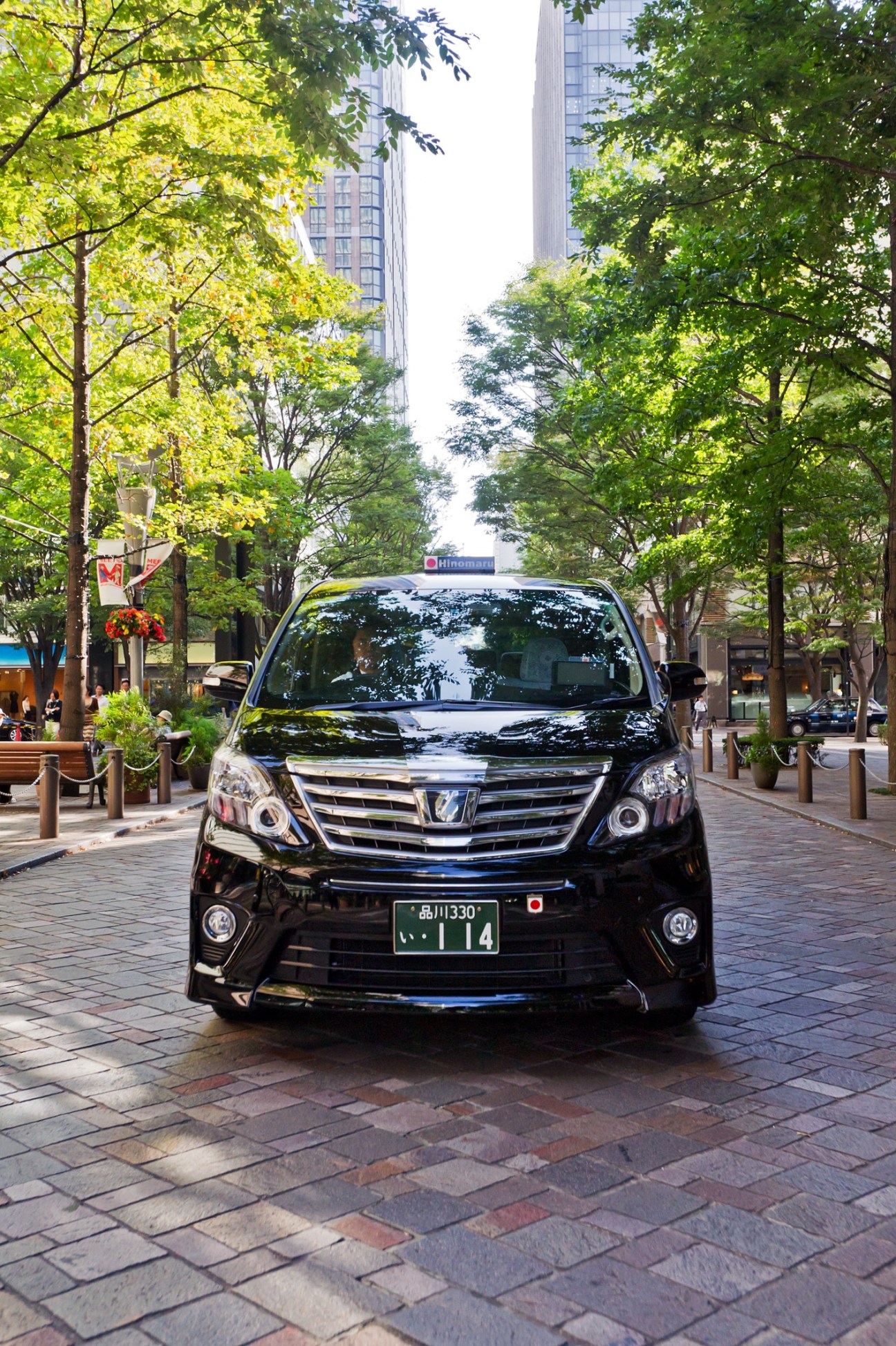 Black Toyota Alphard MPV parked on a tree-lined urban street in Japan