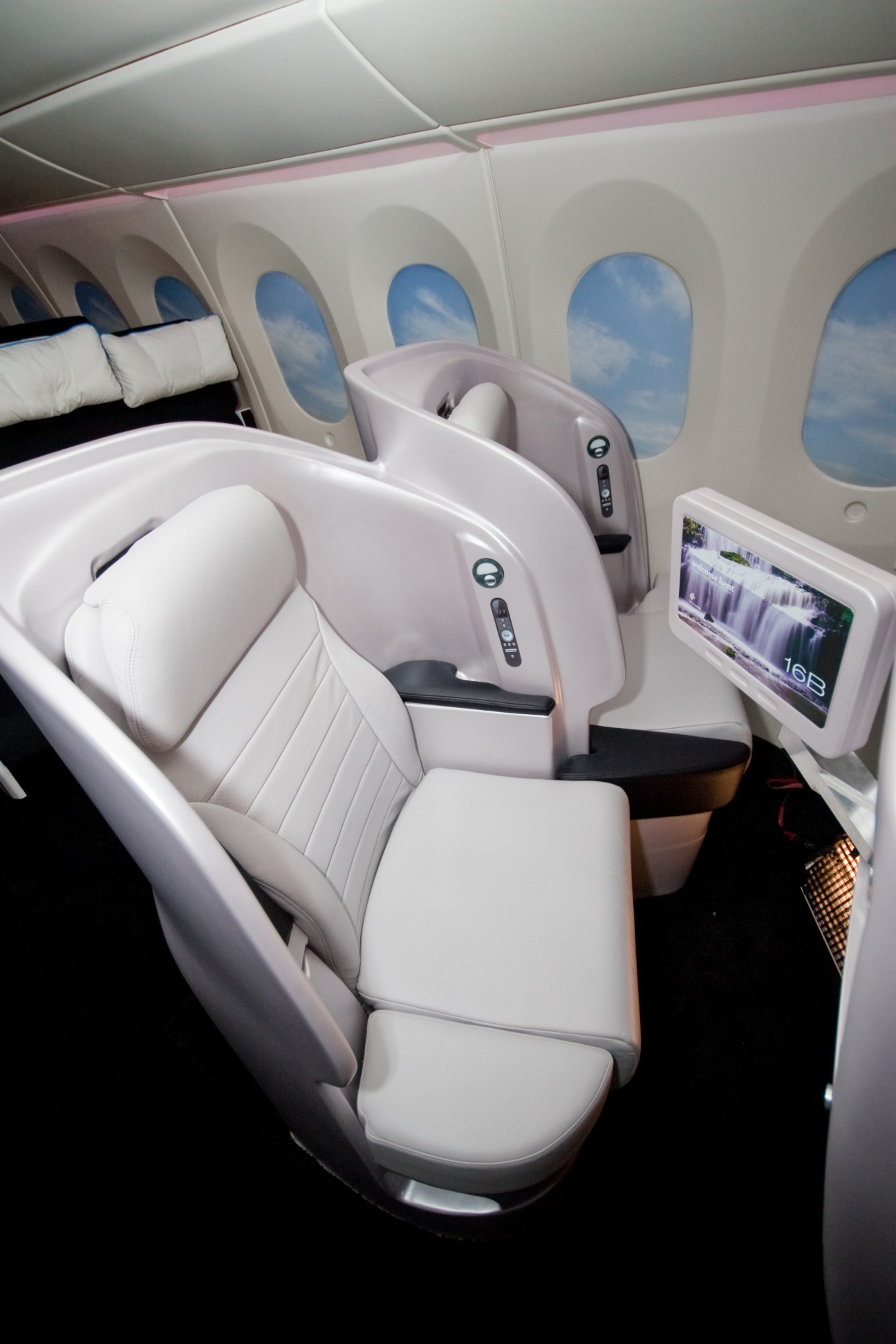 Air New Zealand Business Class lie-flat seat with white leather upholstery and in-flight entertainment screen.