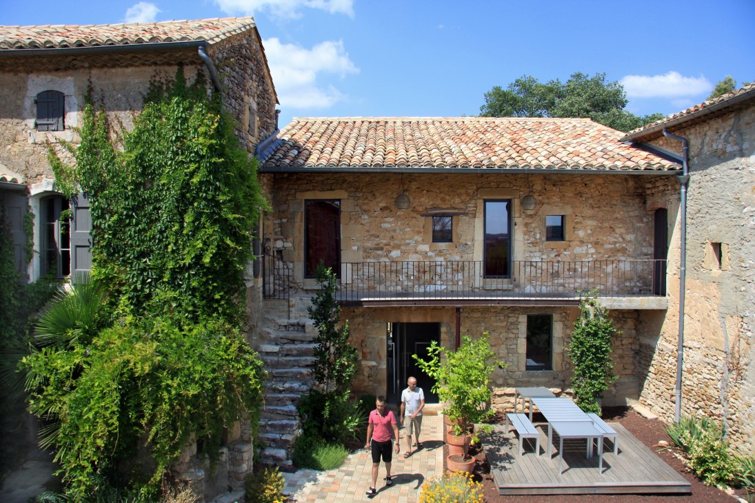 Stone courtyard of La Maison d'Ulysee with ivy-covered walls, terracotta roof, and guests relaxing in the French countryside.