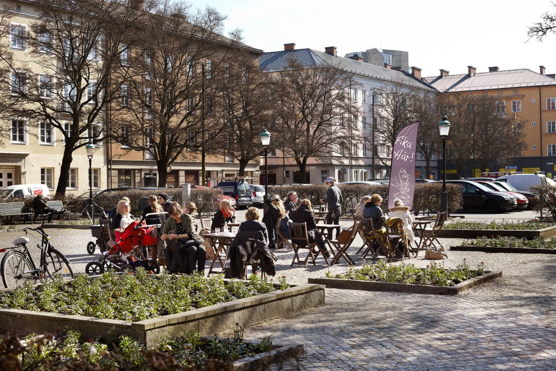 People sitting at outdoor tables in a sunny public square in Malmö with historic buildings in the background.
