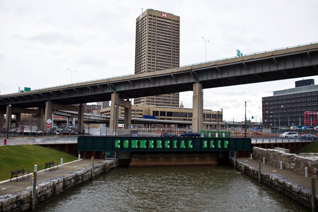 Buffalo's waterfront with Commercial Slip sign beneath highway overpass and grain silos in background.