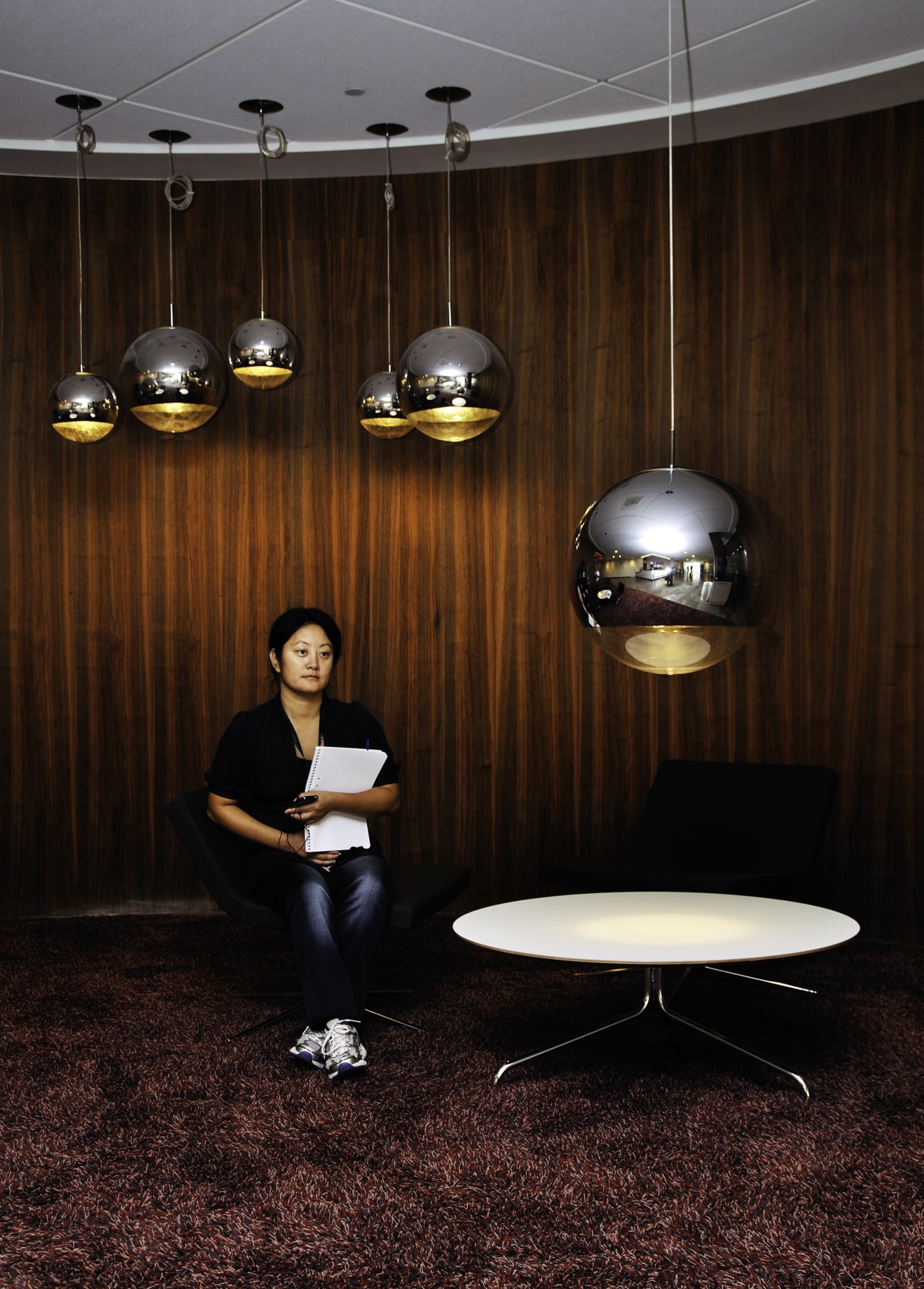 Woman sitting in a modern lobby with wooden paneling and hanging pendant lights.