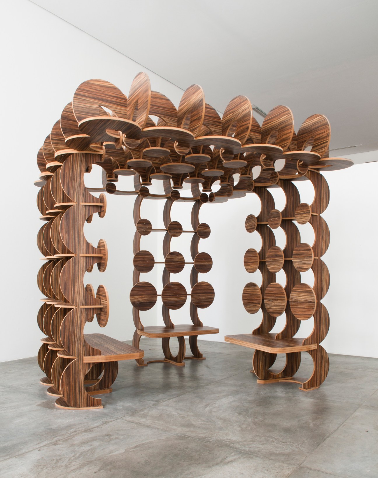Ornate wooden sculptural installation with curved leaf-like panels and circular elements forming an enclosed structure.