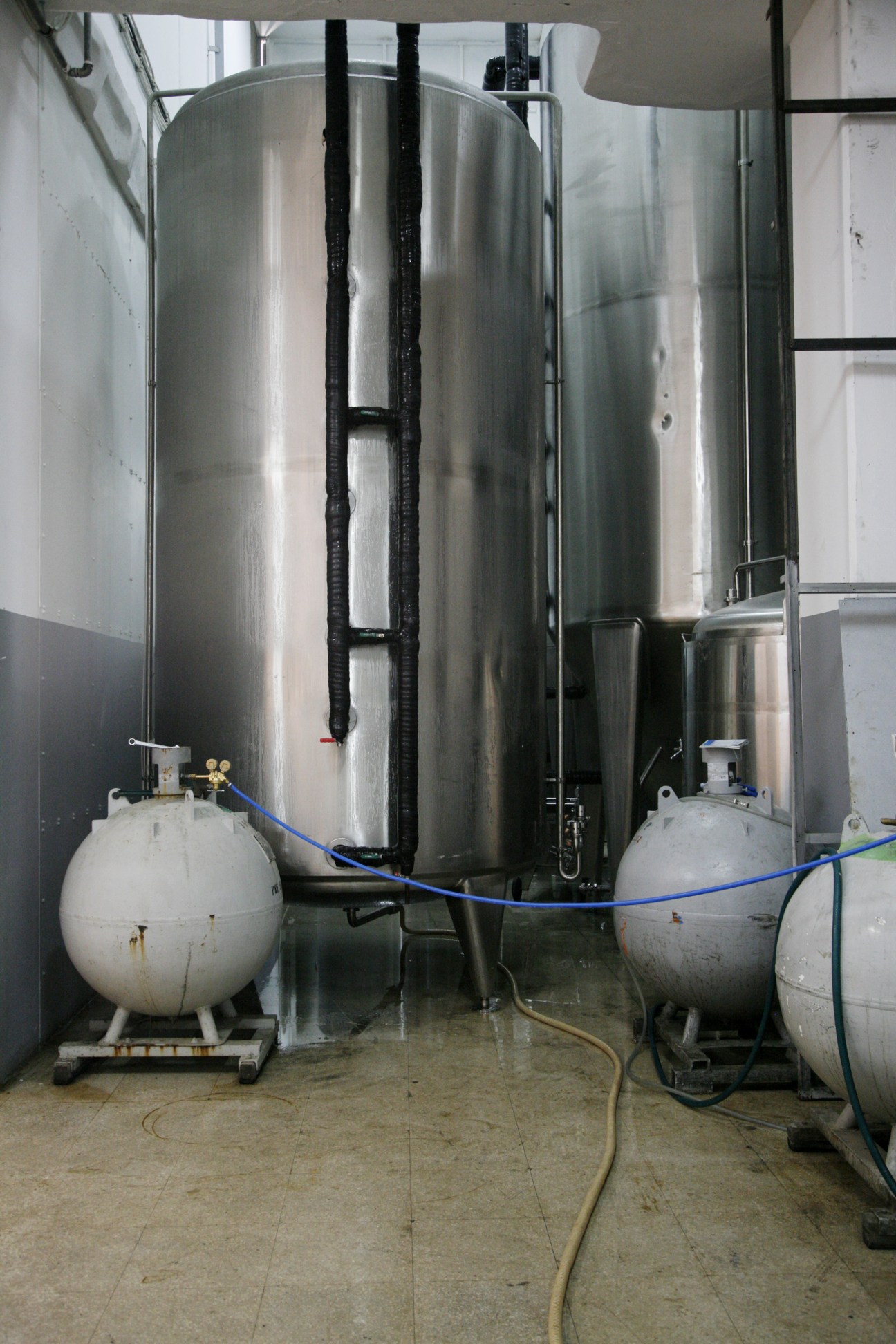 Interior of LB beer brewery showing large metal fermentation tanks and smaller spherical vessels with blue tubing.
