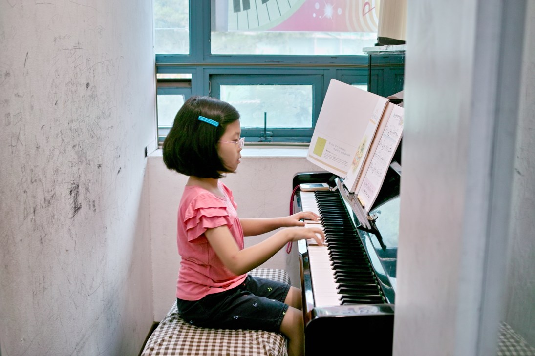Eight-year-old Cho Yun-je plays piano in a small white cubicle at a hagwon cram school.