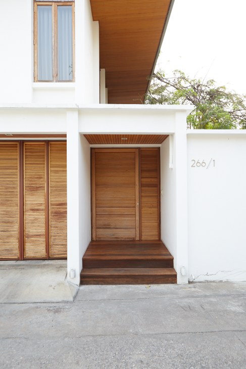 Modern house front entrance with wooden louvered door and shutters on white facade.