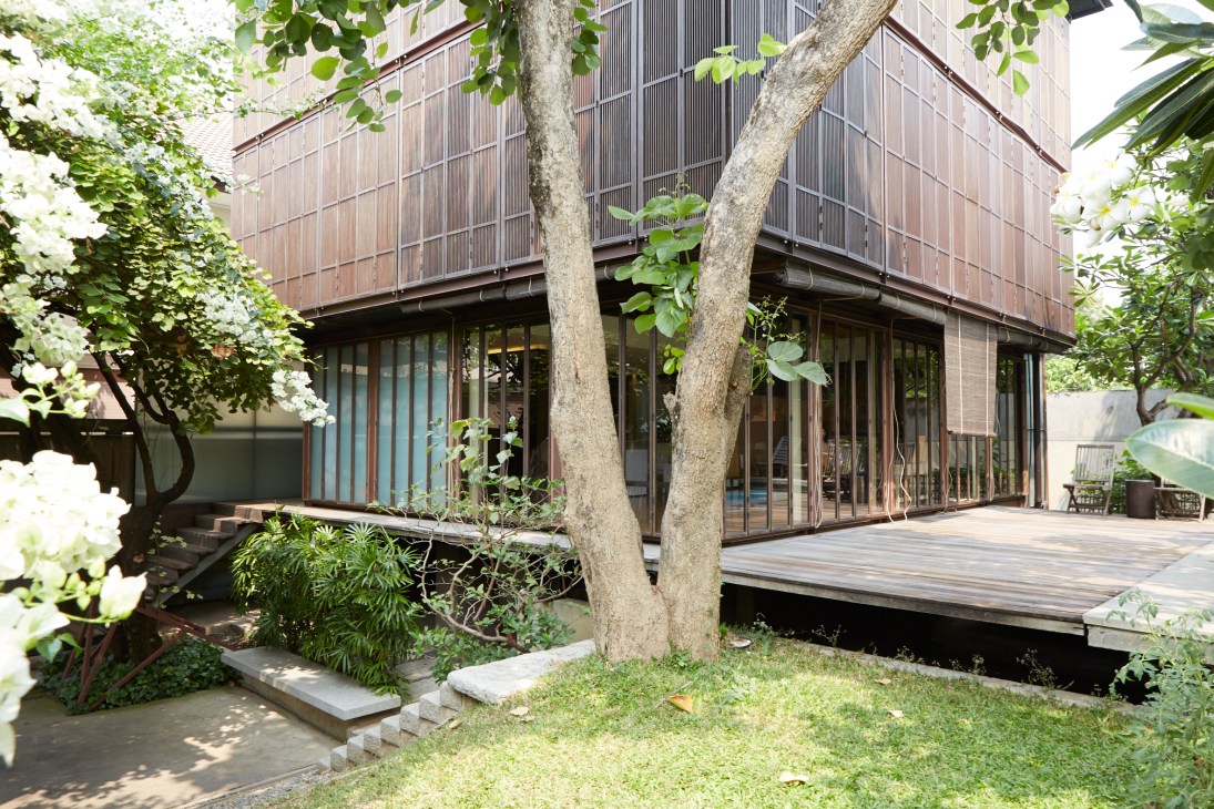 Boon Design's Aurapin House with wooden screening, large windows, and raised foundation surrounded by tropical vegetation.