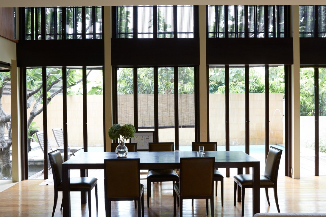 Modern dining area with black wooden chairs around a table, featuring layered black screens and large windows overlooking tropical garden.
