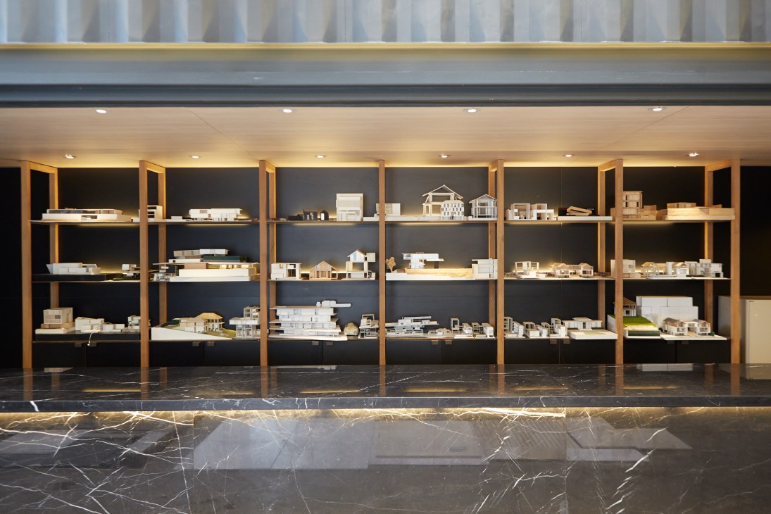 Model archive displaying numerous architectural scale models on illuminated wooden shelves in Boon Design office.