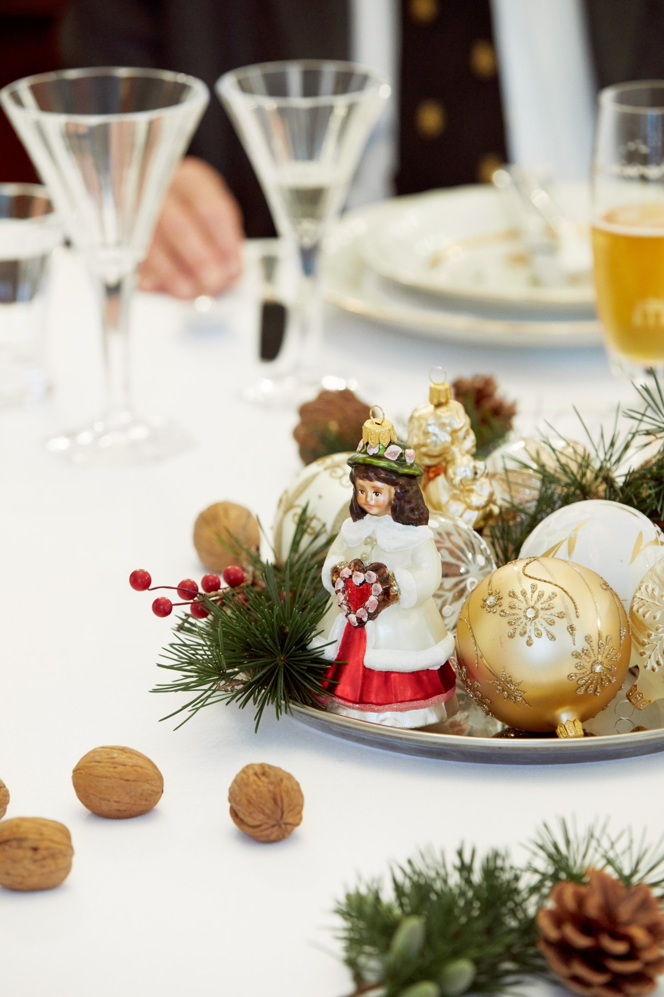Festive table setting with champagne glasses, gold and white Christmas ornaments, and decorative figurine.