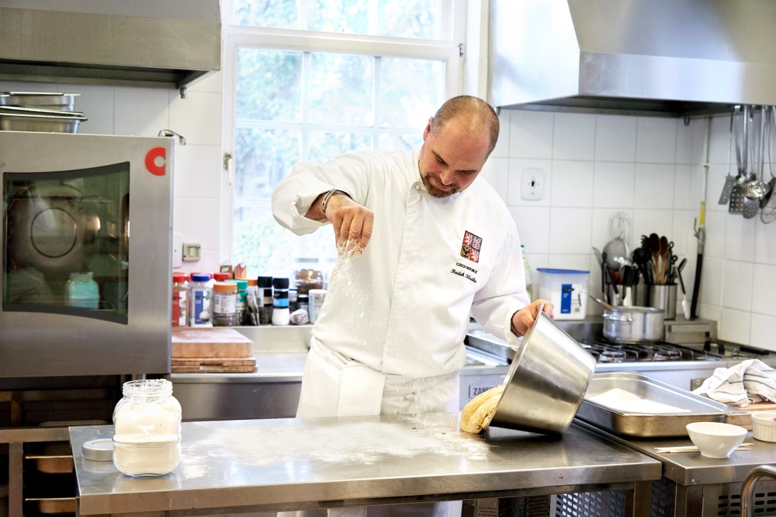Chef Radek Kludka pouring dough into a metal pot in a bright kitchen.