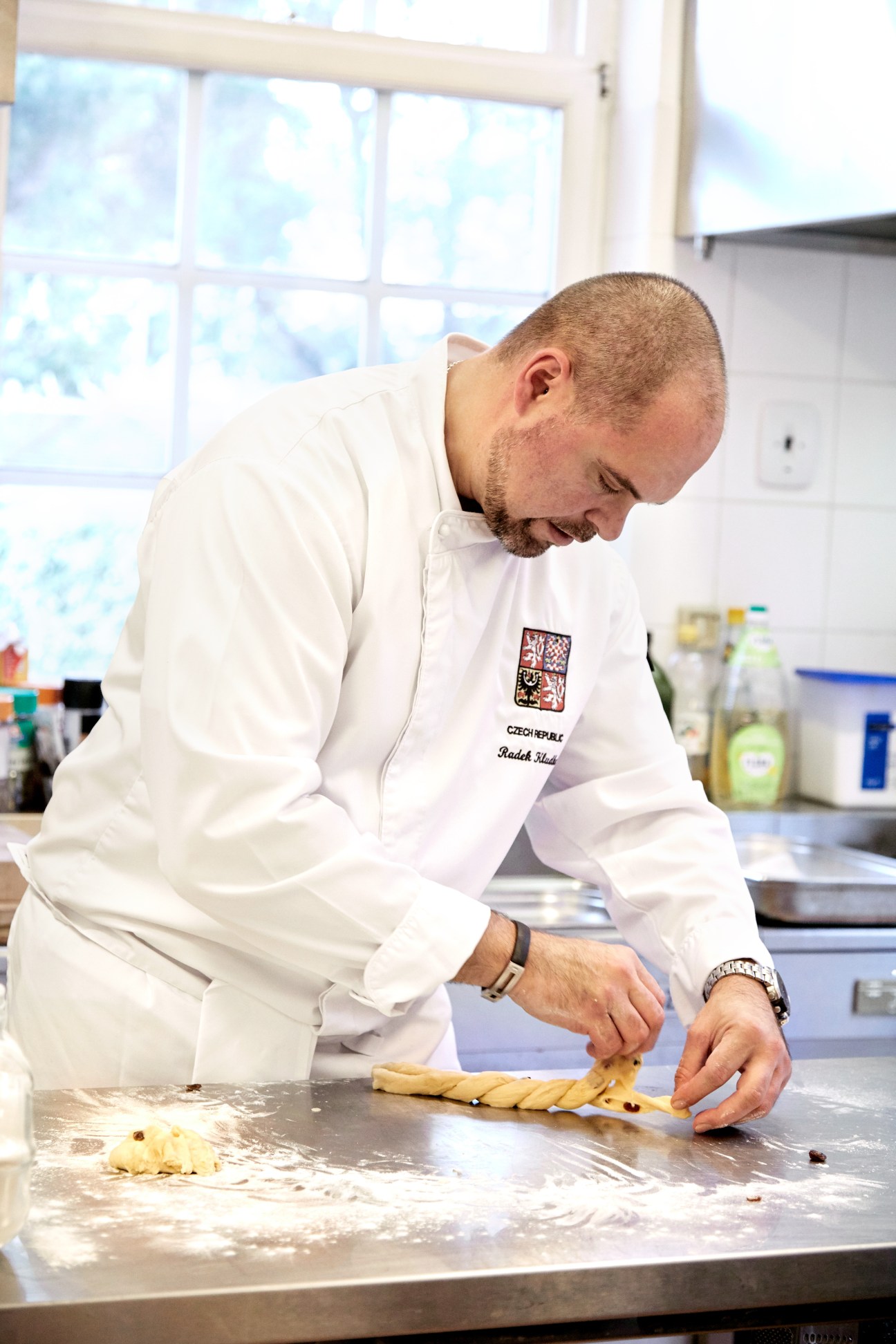 Chef Radek Kludka braiding dough for traditional Czech Christmas cake vanocka in a bright kitchen.