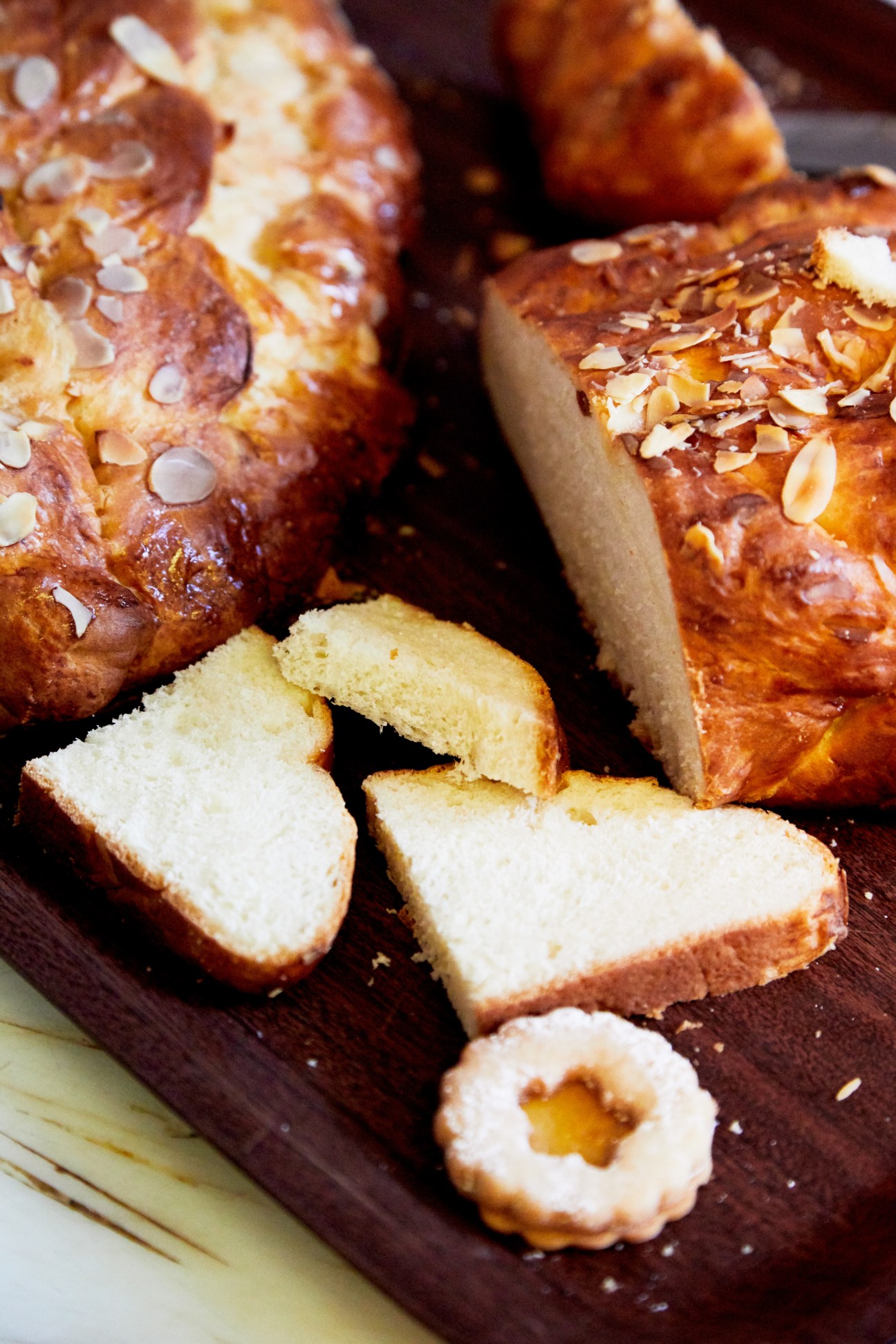Sliced Czech vanocka braided Christmas cake with almonds on a dark wooden board.