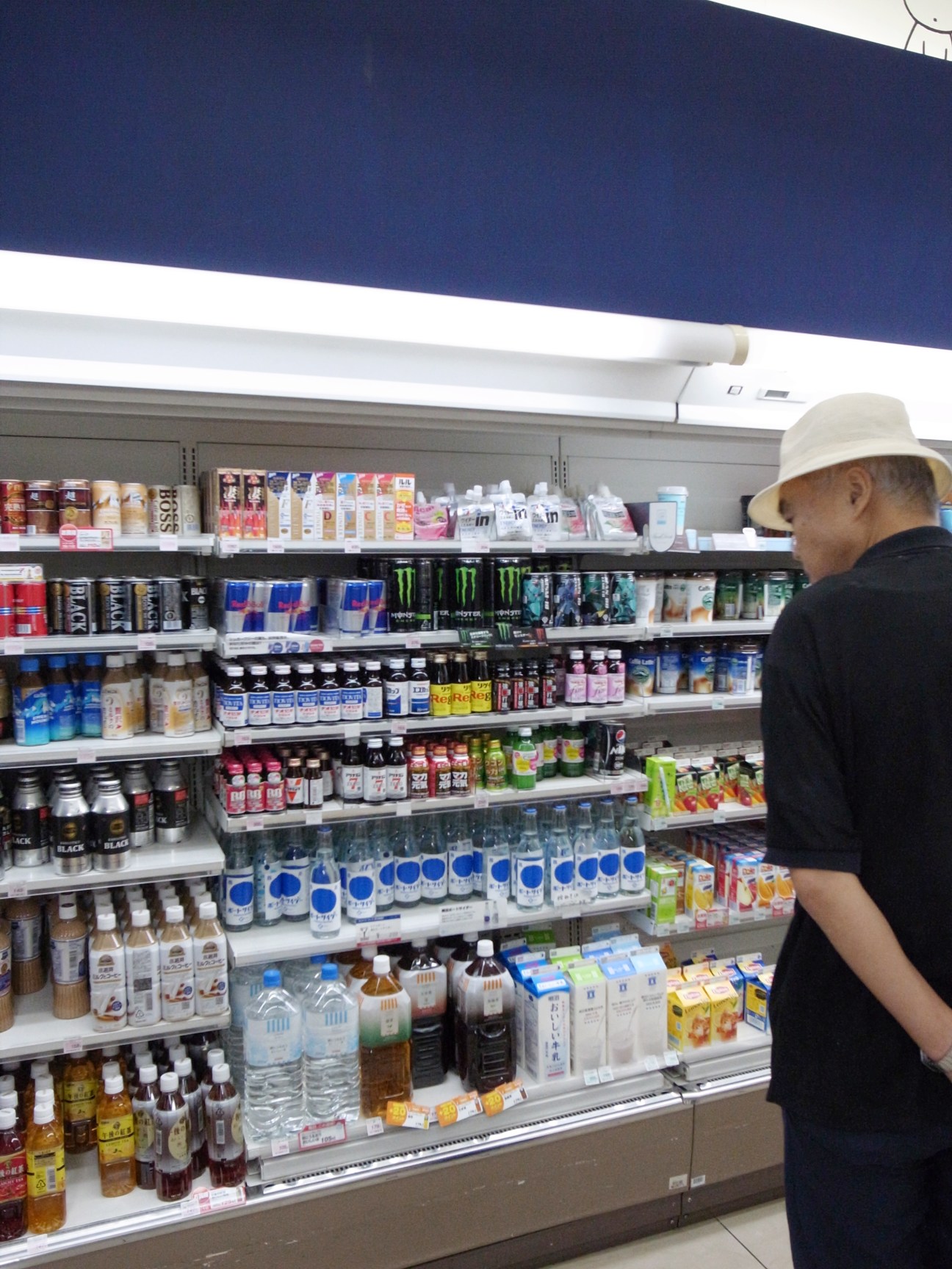 Man in white hat browsing a refrigerated display shelf stocked with colorful bottles of nutrition and energy drinks.