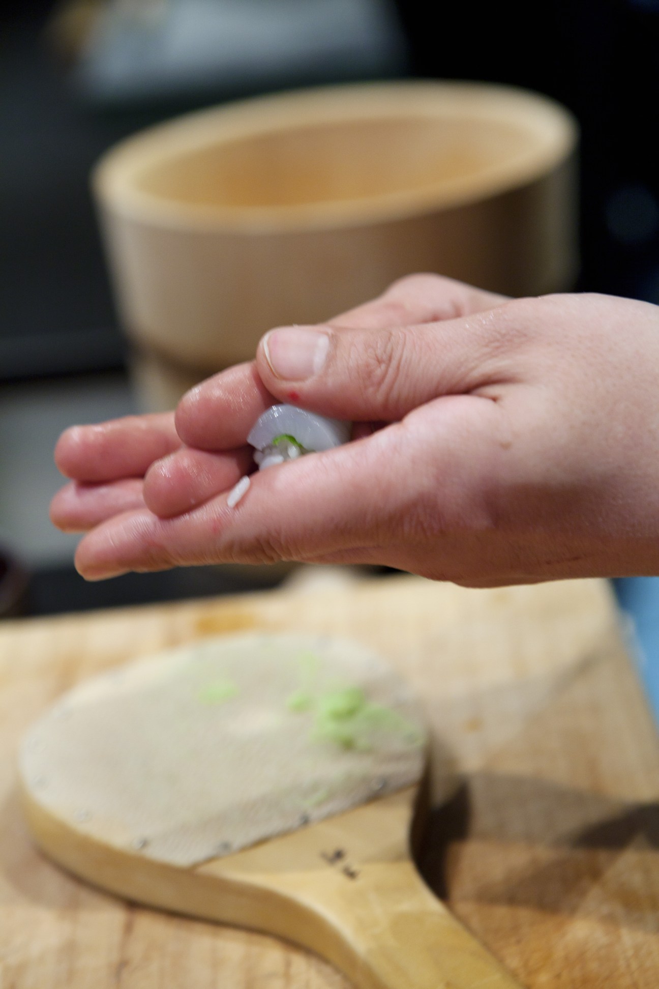 Chef's hand holding a piece of sushi with rice and fish during preparation.