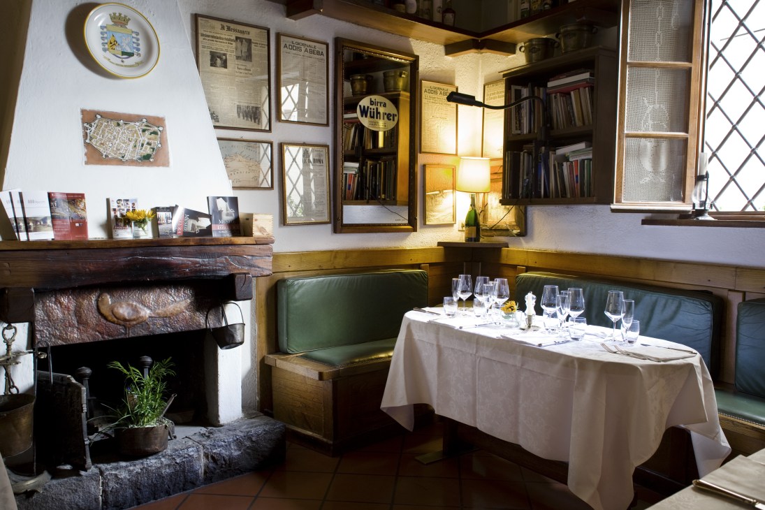 Cosy dining room at Buca di Sant'Antonio with fireplace, green banquette seating, and white tablecloth.