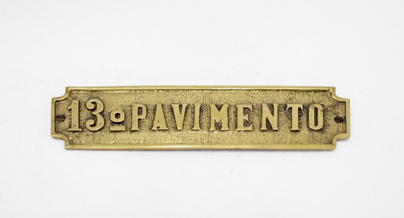 Brass door plaque reading '13º PAVIMENTO' (13th floor) against white background.